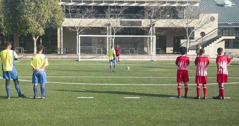 Youth soccer teams facing penalty kick on school field in sunny weather