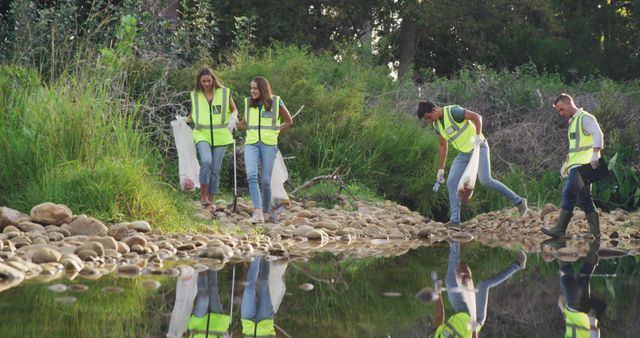 Group of volunteers participating in an outdoor cleanup effort along a riverbank. They are wearing protective gear and working together to clean up the environment. Ideal for campaigns, articles, and promotions focused on environmental conservation, community service, eco-friendly activities, and teamwork initiatives.