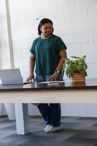 African american woman standing at desk using laptop in minimalist daylight workspace