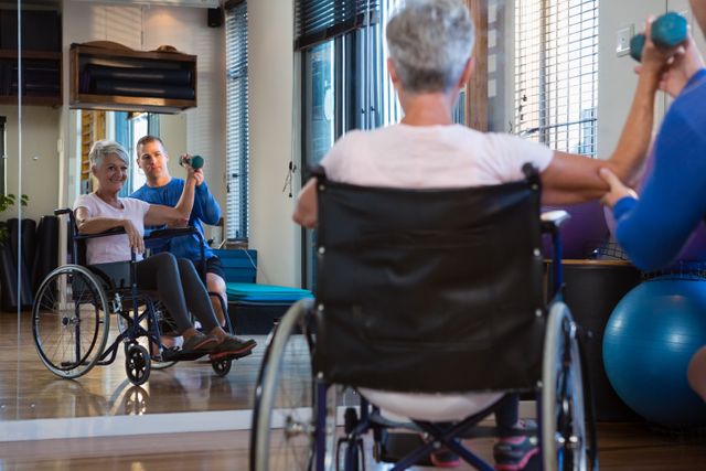 Image shows a physiotherapist assisting a wheelchair-bound patient with exercise using a dumbbell in a clinical setting. Useful for promoting physical therapy services, medical practices focused on rehabilitation, and healthcare facilities that cater to elderly care or individuals with mobility challenges.
