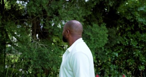 Man standing in garden turning head left among lush green foliage and red flowers