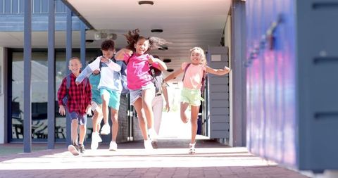 Diverse group of happy students running excitedly in school corridor