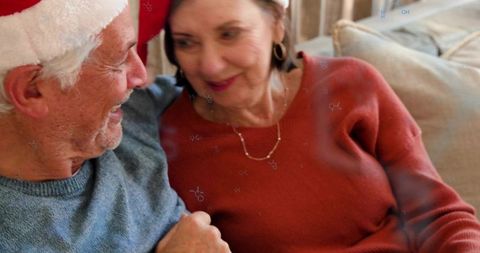 Senior couple sharing cozy holiday moment on couch wearing santa hats and knit sweaters