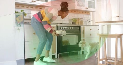 Removing baking dish from oven in cozy sunlit kitchen while dog watches