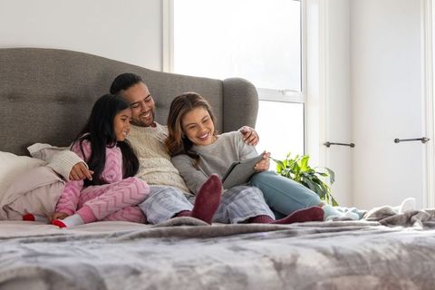 Cozy family morning cuddling on bed watching tablet in pajamas, parents and daughter bonding