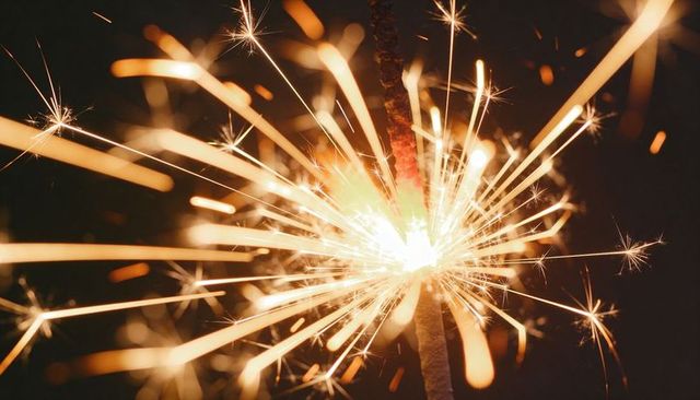 Handheld Sparkler Burning and Radiating Golden Sparks Against Dark Night Backdrop