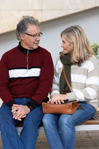 Senior couple sharing quiet moment on bench in plaza wearing cozy sweaters and scarf