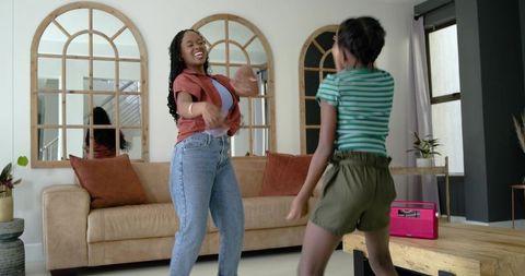 African-american mother and teen daughter hugging and laughing in cozy modern living room
