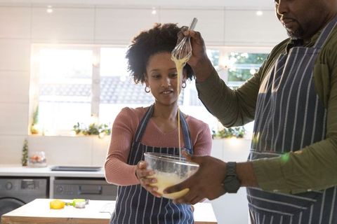 African american father and teen daughter baking together mixing batter in sunlit kitchen
