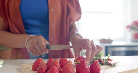 African american woman slicing strawberries on cutting board in sunlit kitchen