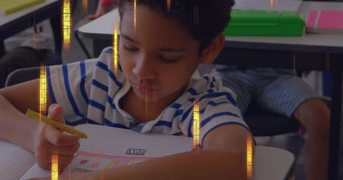 Concentrating schoolboy coloring lined notebook at classroom desk with yellow pencil