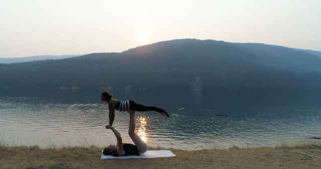 Couple engaged in acro yoga exercise on lakeside during sunset offers a calming and serene depiction of balance and teamwork. Perfect for usage in wellness, fitness, nature retreats, yoga promotions, and couples dynamics content.