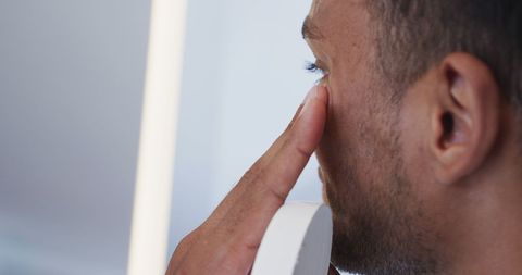 Biracial Man Applying Face Cream in Bathroom Mirror