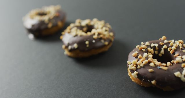 Three delicious chocolate donuts with nut toppings on a black background. Perfect for illustrating concepts of indulgence, snack time, or showcasing bakery products. Great for food blogs, menus, and advertisements focused on sweets and treats.