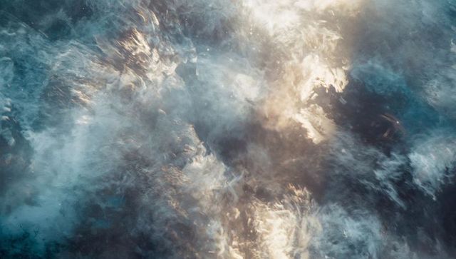 Aerial turbulent ocean waves and white foam catching golden sunlight, abstract texture