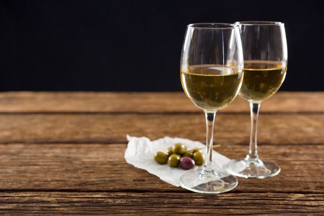 Close-up of olives with glasses of wine on table