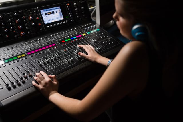 Female audio engineer adjusting sound mixer in recording studio. Ideal for illustrating concepts related to music production, sound engineering, professional audio work, and the music industry. Useful for articles, blogs, and promotional materials about careers in audio engineering and studio technology.