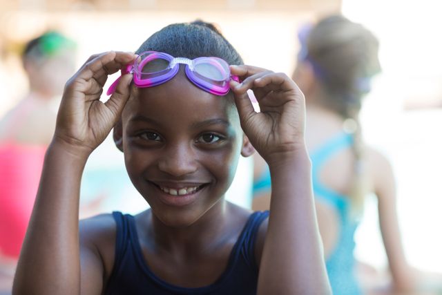 Close up portrait of smiling girl holding swimming goggles at poolside
