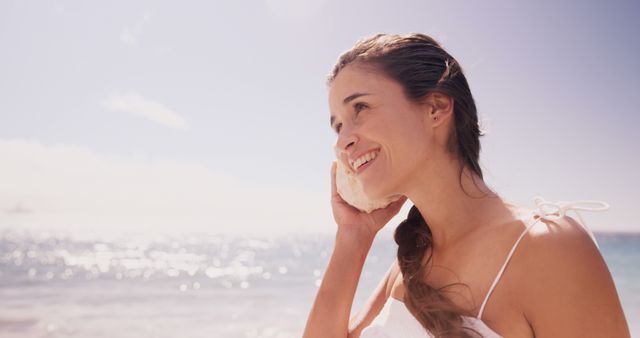 Woman in Sundress Smiling at Beach with Seashell Near Ear - Download Free Stock Images Pikwizard.com