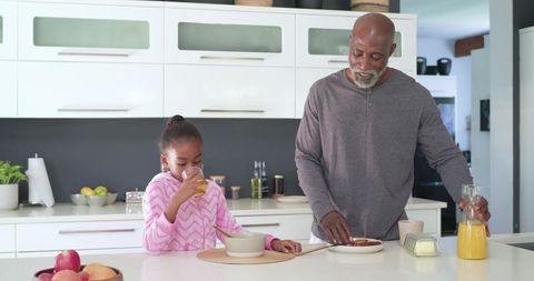 African american grandfather and granddaughter sharing breakfast in modern bright kitchen