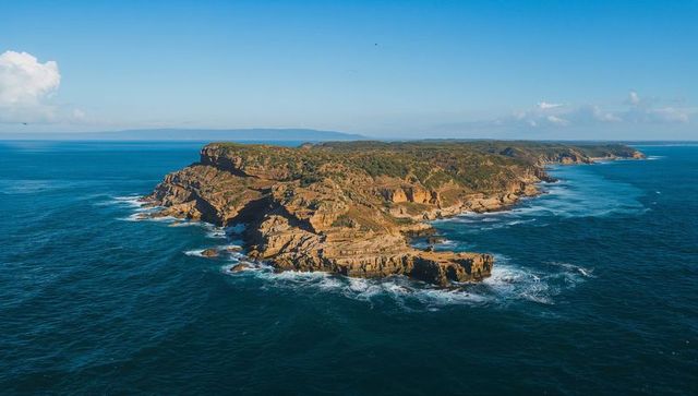 Aerial sandstone headland jutting into deep blue ocean, rugged cliffs and surf