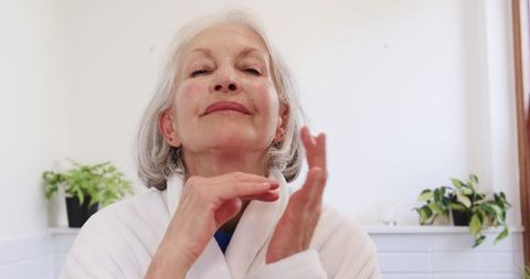 Senior Woman Applying Facial Cream in Bathroom with Greenery Touch
