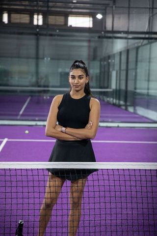 Indian woman standing arms crossed on purple indoor tennis court exuding confidence