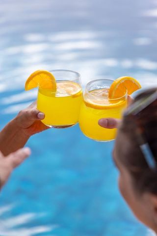 Poolside clinking glasses with orange cocktails and citrus garnish for summer cheers