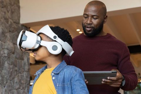 African American Father Supervising Son Using VR Headset Holding Tablet in Living Room