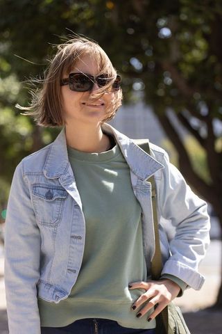 Wind-blown young woman standing on urban sidewalk wearing denim jacket and sunglasses