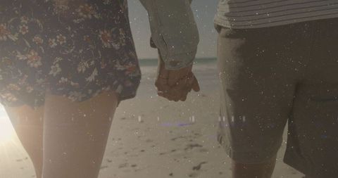 Sunlit couple walking hand in hand on sandy shore at golden hour