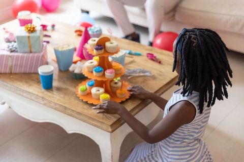 Child with dreadlocks reaching cupcake tower at indoor birthday celebration