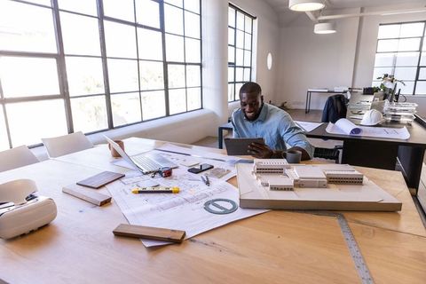 African american architect working on tablet in bright design studio with model and plans