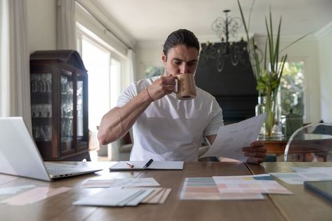 Freelance Designer Reviewing Charts and Color Swatches While Drinking Coffee at Home Workspace