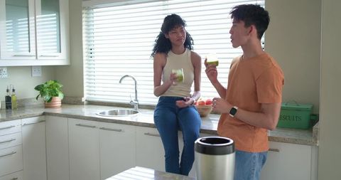 Young multicultural couple enjoying green smoothies and chatting in bright modern kitchen