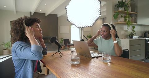 Diverse female cohosts recording podcast with laptop, microphone and studio lighting