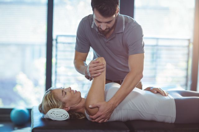 Physiotherapist treating a woman's shoulder in a clinic. Ideal for use in healthcare, rehabilitation, and wellness content. Can be used in articles, blogs, or advertisements related to physical therapy, injury recovery, and medical treatments.