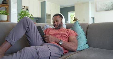 Mature african american man relaxing on sofa with headphones and tablet in modern living room
