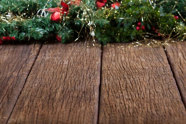 Christmas garland with fir branches, red berries, and gold tinsel on a rustic wooden plank. Ideal for holiday-themed designs, festive invitations, seasonal promotions, and Christmas decorations.