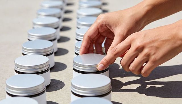 Hands placing silver-lid jars in sunlight rows repeating pattern for packaging mockup