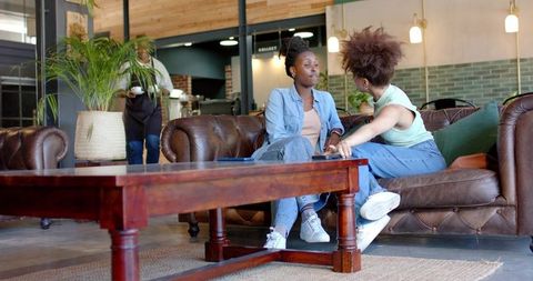 Two women chatting on leather sofa in modern cafe lounge casual friendship moment