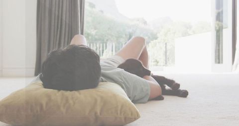 Man lounging on sunlit carpet near patio door with dog and pillow, cozy home relaxation