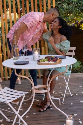 Candlelit backyard bistro date kissing forehead at twilight with wine and charcuterie
