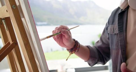 Indian artist painting on lakeside balcony wearing headphones plein air