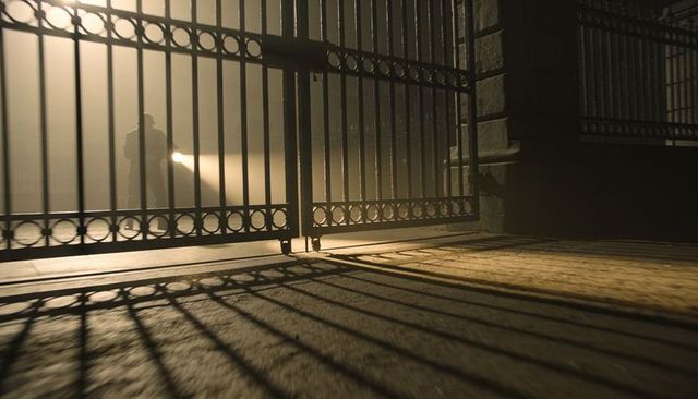 Security guard with flashlight inspecting wrought-iron gate in foggy night, dramatic backlight