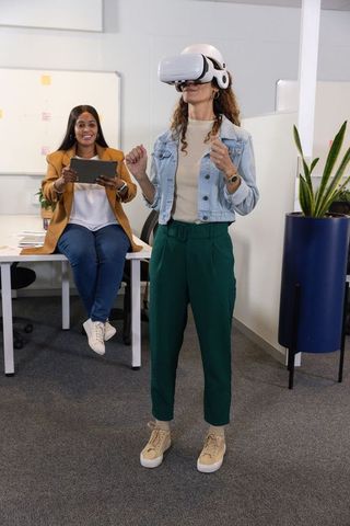 Diverse female coworkers testing virtual reality headset for collaborative training in office