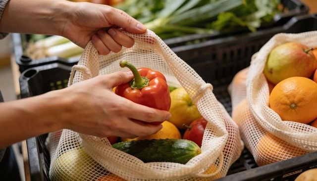Selecting red bell pepper using reusable mesh bag while grocery shopping for fresh produce