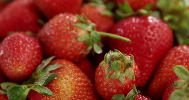Close-up view of fresh, ripe strawberries with green leaves perfect for illustrating the freshness and vibrancy of organic fruits. Useful for advertising healthy eating, vegan recipes, summer fruit themes, and food-related blogs and articles.