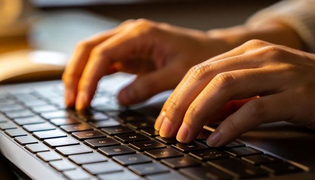 Close-up of hands typing on laptop keyboard in warm home office lighting for remote work