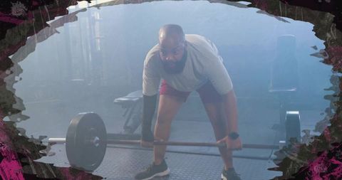 Bearded man lifting heavy barbell deadlift in hazy gym wearing elbow sleeve and smartwatch